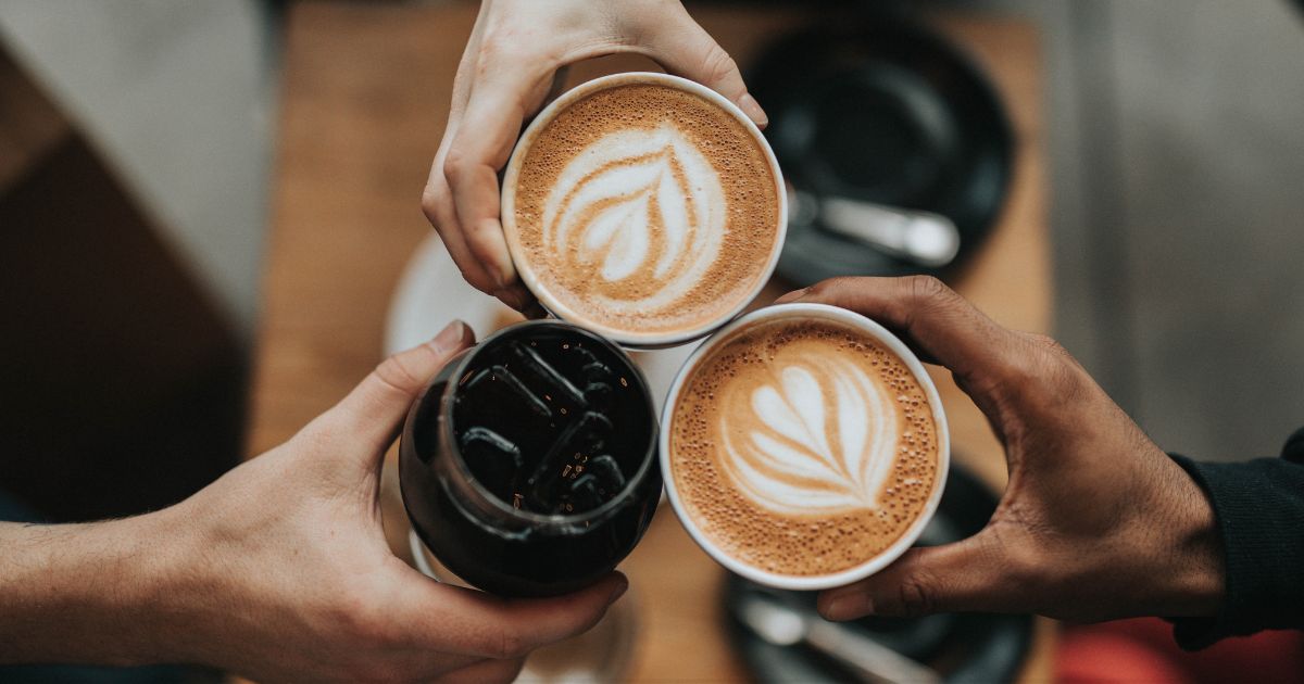 A close up of three hands holding three cups of coffee.